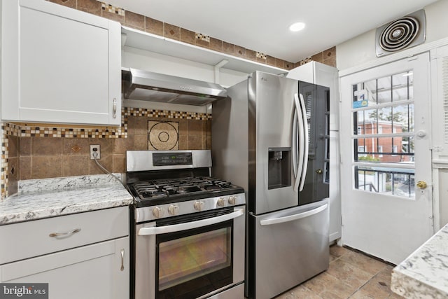 kitchen with appliances with stainless steel finishes, wall chimney range hood, tasteful backsplash, white cabinetry, and light stone counters