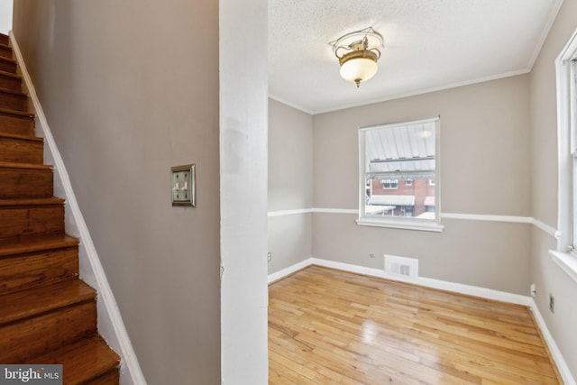 unfurnished room with stairs, wood finished floors, baseboards, crown molding, and a textured ceiling