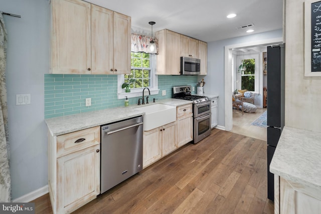 kitchen featuring appliances with stainless steel finishes, light brown cabinetry, a sink, dark wood-style floors, and backsplash