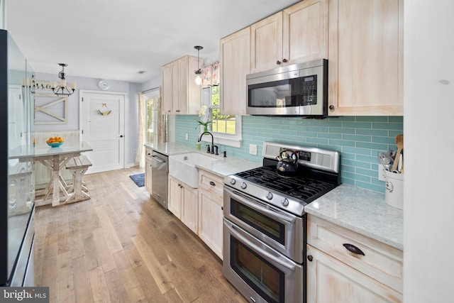 kitchen featuring stainless steel appliances, a sink, light brown cabinets, and tasteful backsplash
