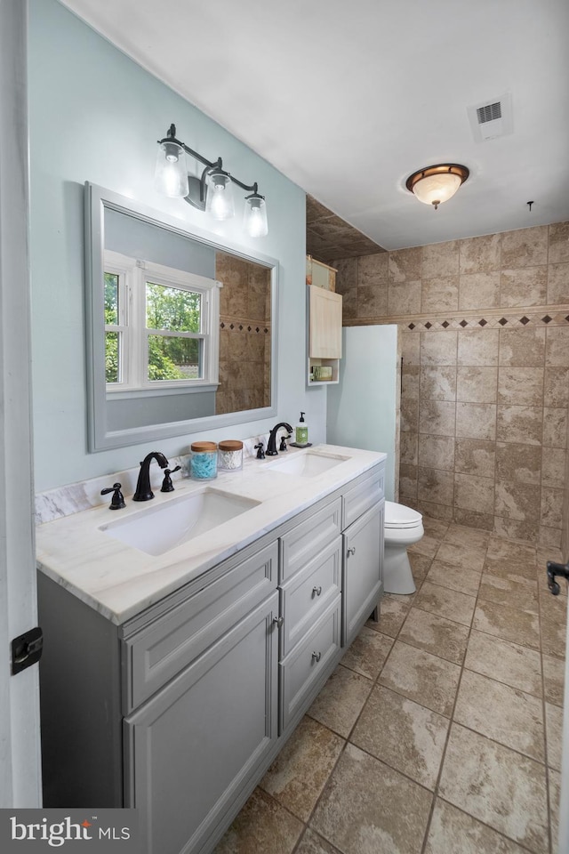 bathroom with double vanity, tiled shower, and toilet