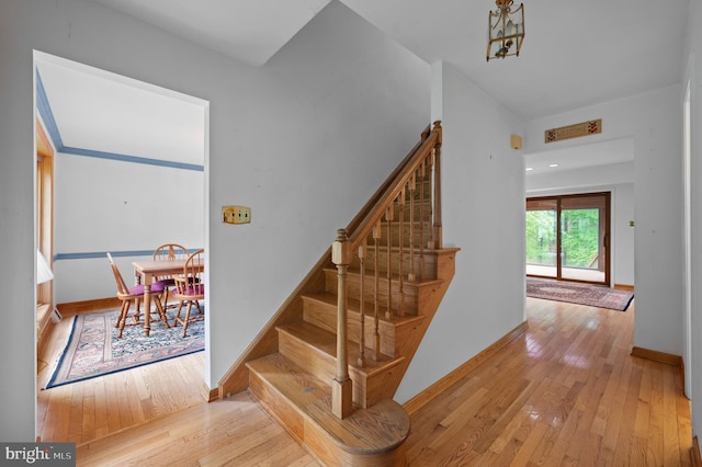 stairs featuring hardwood / wood-style flooring, baseboards, and a chandelier