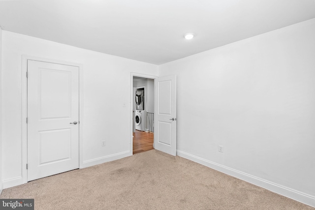 unfurnished bedroom featuring stacked washing machine and dryer, carpet, and baseboards