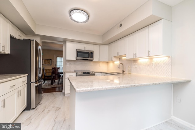 kitchen featuring appliances with stainless steel finishes, a peninsula, white cabinets, and light stone countertops