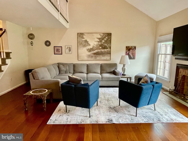 living area with stairs, wood finished floors, high vaulted ceiling, baseboards, and a fireplace
