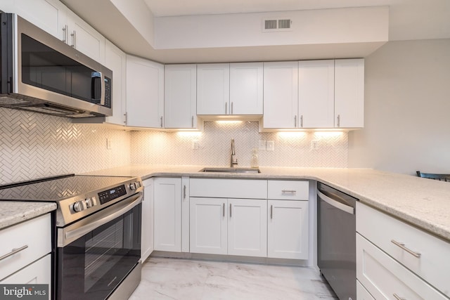 kitchen featuring appliances with stainless steel finishes, a sink, light marble finish flooring, tasteful backsplash, and white cabinetry