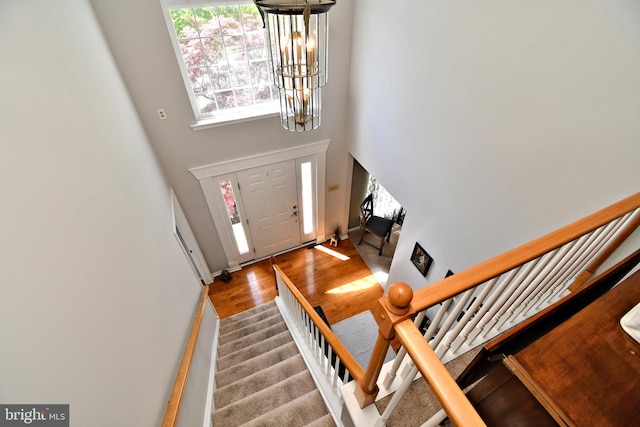 foyer entrance with wood finished floors, stairway, a towering ceiling, a chandelier, and baseboards