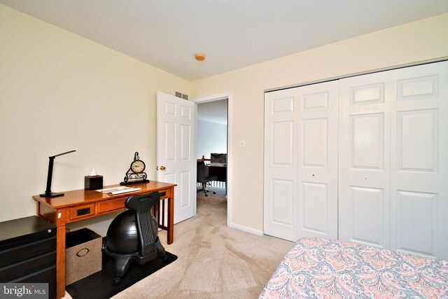 bedroom with light colored carpet, a desk, a closet, and baseboards