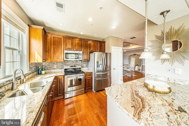 kitchen with appliances with stainless steel finishes, a sink, wood finished floors, decorative backsplash, and light stone countertops