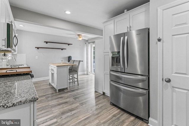 kitchen with stainless steel appliances, butcher block countertops, a sink, white cabinets, and light wood-style floors