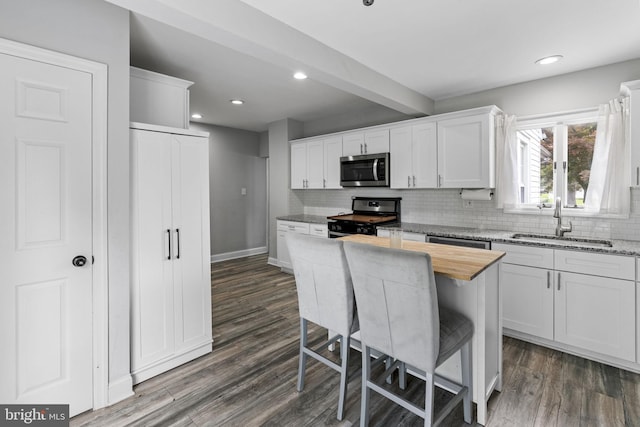 kitchen featuring stove, a sink, stainless steel microwave, backsplash, and dark wood-style flooring