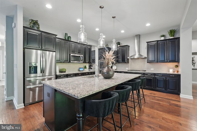 kitchen featuring stainless steel appliances, wall chimney exhaust hood, a sink, light stone countertops, and backsplash
