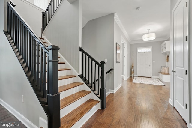 foyer featuring ornamental molding, wood finished floors, baseboards, and stairway