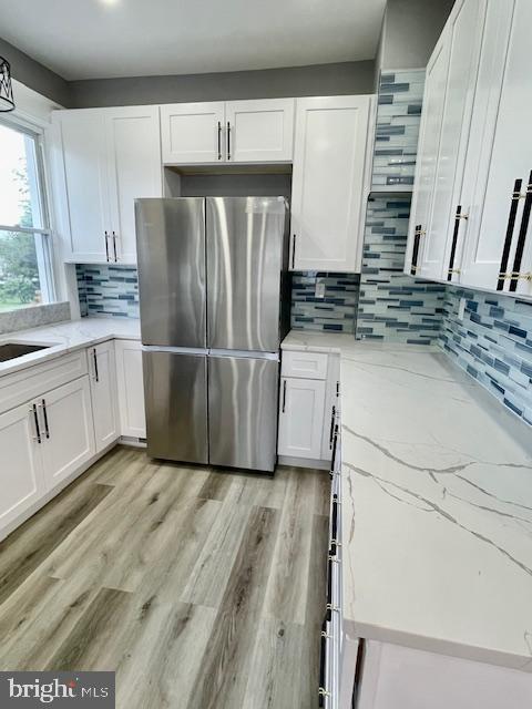 25 Elmont Ave, Baltimore, MD 21206 - kitchen with freestanding refrigerator, white cabinetry, light stone counters, tasteful backsplash, and light wood-style floors