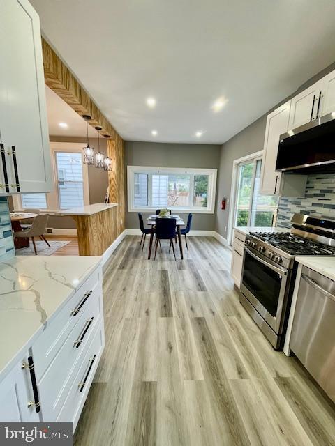 25 Elmont Ave, Baltimore, MD 21206 - kitchen with appliances with stainless steel finishes, white cabinetry, decorative backsplash, light wood-style floors, and light stone countertops