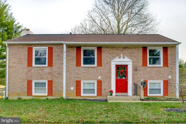 split foyer home featuring a front yard, brick siding, a chimney, and roof with shingles
