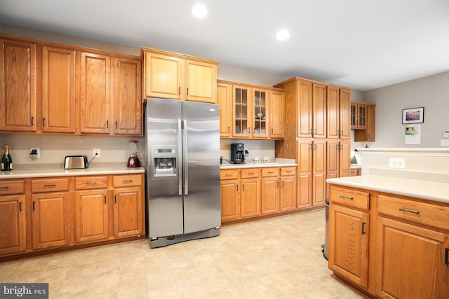 kitchen featuring stainless steel fridge, light countertops, brown cabinets, glass insert cabinets, and recessed lighting
