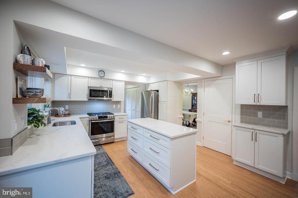 kitchen featuring appliances with stainless steel finishes, open shelves, a sink, light wood-style flooring, and tasteful backsplash
