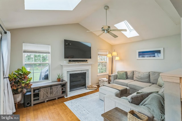 living room featuring a skylight, lofted ceiling, healthy amount of natural light, wood finished floors, and a high end fireplace