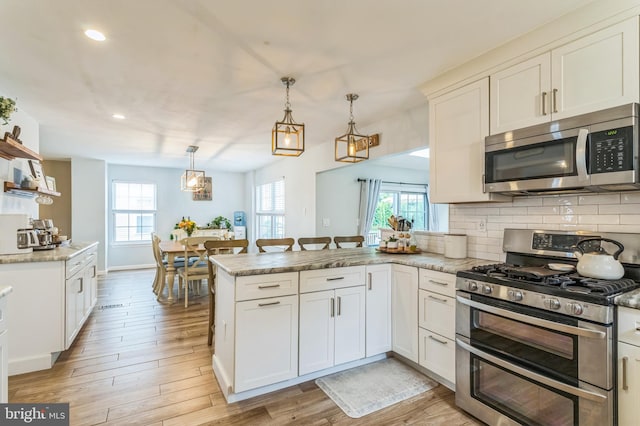 kitchen with appliances with stainless steel finishes, a peninsula, backsplash, light wood-style floors, and white cabinets