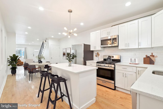 kitchen featuring stainless steel appliances, a center island, a chandelier, tasteful backsplash, and light wood finished floors