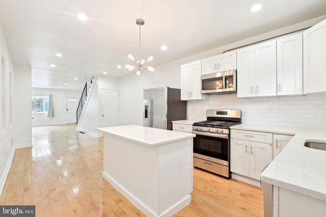 kitchen featuring appliances with stainless steel finishes, a kitchen island, tasteful backsplash, a chandelier, and light wood-style flooring