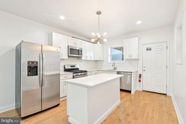 kitchen featuring appliances with stainless steel finishes, backsplash, light wood-type flooring, white cabinets, and a chandelier