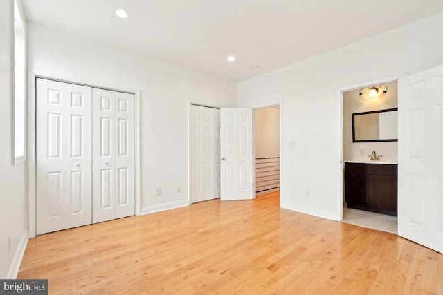 unfurnished bedroom featuring multiple closets, light wood finished floors, baseboards, connected bathroom, and recessed lighting