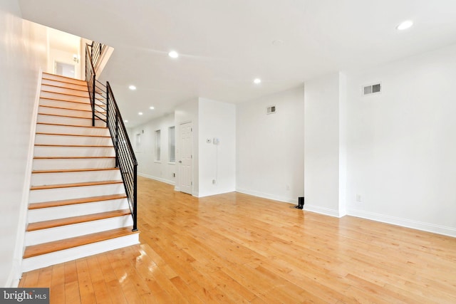 unfurnished living room featuring baseboards, stairs, light wood-style flooring, and recessed lighting