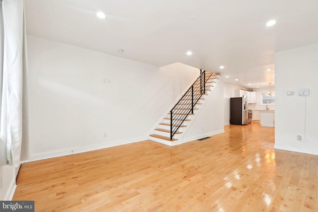 unfurnished living room featuring light wood finished floors, stairs, recessed lighting, and baseboards