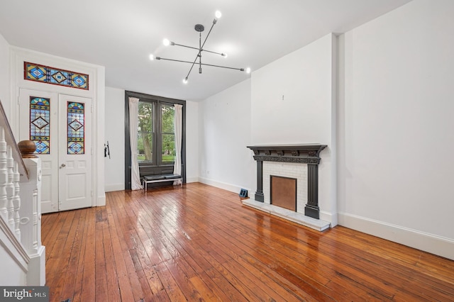unfurnished living room featuring hardwood / wood-style floors, a chandelier, baseboards, and a brick fireplace