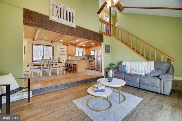 living room with wood finished floors, a ceiling fan, recessed lighting, stairs, and beamed ceiling