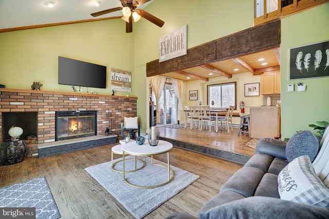 living area featuring a ceiling fan, wood finished floors, a brick fireplace, and high vaulted ceiling