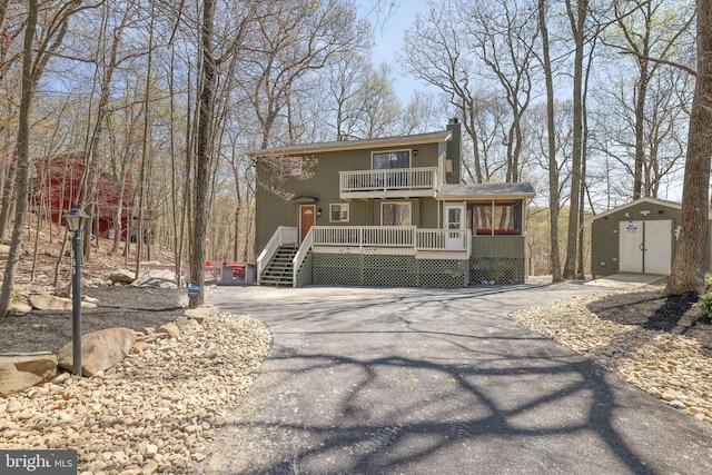 view of front of property with a balcony, a chimney, driveway, an outbuilding, and a storage shed