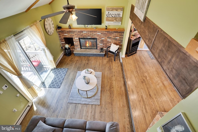 living room with a fireplace, a ceiling fan, wood finished floors, and a baseboard heating unit
