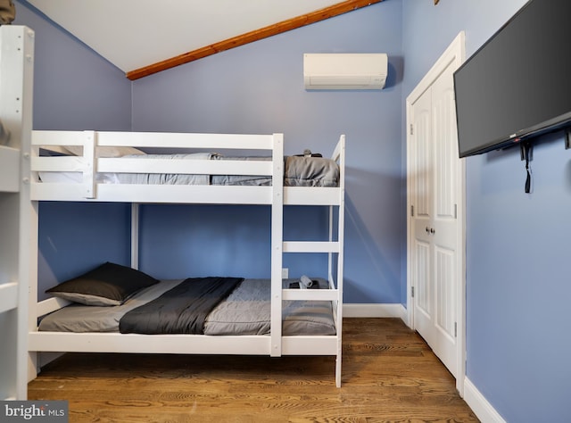 bedroom with a wall mounted AC, lofted ceiling, and wood finished floors