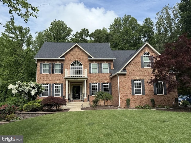colonial home with brick siding, a front lawn, and a balcony