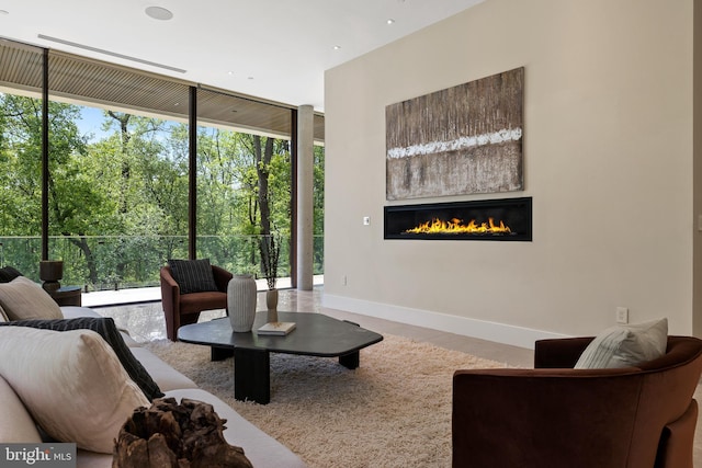 living room featuring a glass covered fireplace, a wall of windows, and baseboards