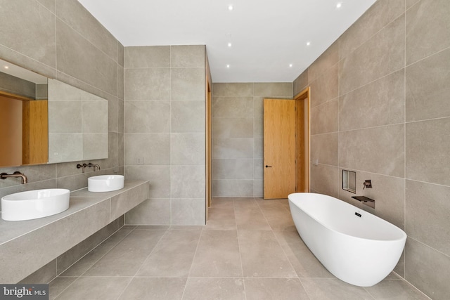 full bath with tile walls, tile patterned flooring, a freestanding tub, and double vanity