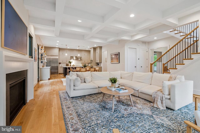 living room featuring light wood finished floors, recessed lighting, stairs, beam ceiling, and a glass covered fireplace