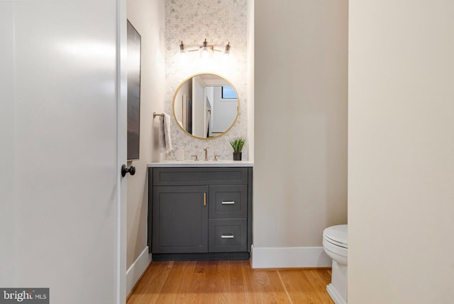 half bath with wood finished floors, toilet, vanity, and baseboards