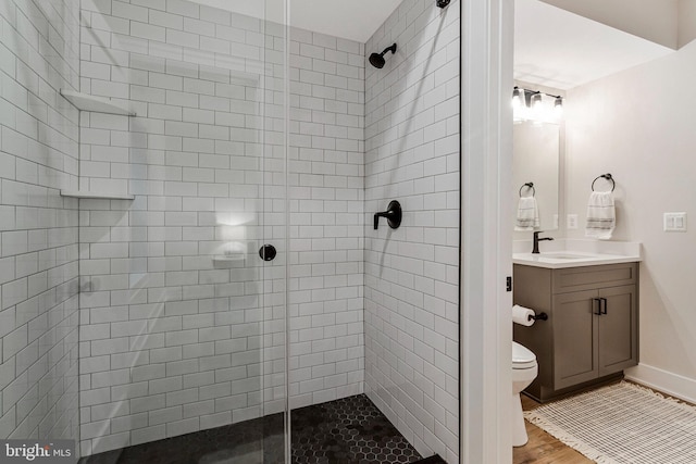 full bathroom with a stall shower, toilet, vanity, wood finished floors, and baseboards