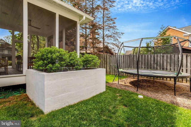 view of yard with a trampoline, fence, and a sunroom