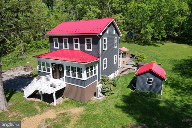 rear view of house featuring a wooden deck, metal roof, a lawn, and a wooded view