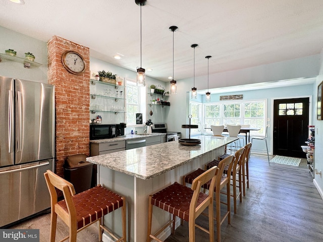 kitchen with appliances with stainless steel finishes, light stone countertops, open shelves, a kitchen bar, and light wood finished floors