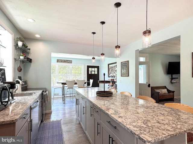 kitchen with stainless steel appliances, wood finished floors, light stone counters, pendant lighting, and a center island