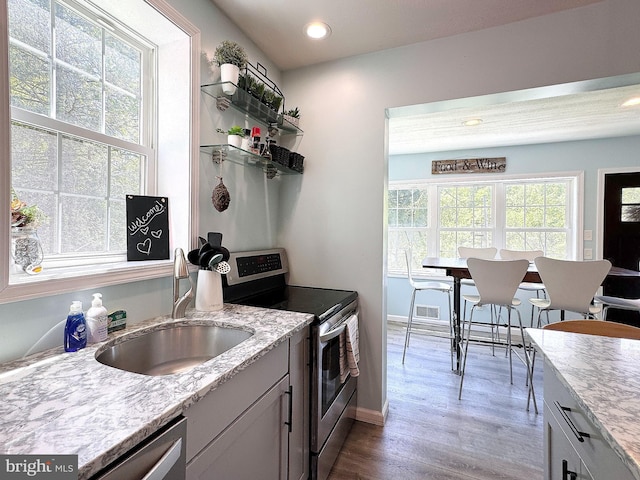kitchen with appliances with stainless steel finishes, a sink, wood finished floors, light stone countertops, and recessed lighting