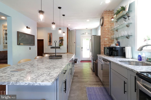 kitchen with a sink, stainless steel appliances, a kitchen island, open shelves, and light wood-style floors