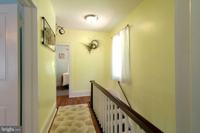 hallway with an upstairs landing, wood finished floors, and baseboards