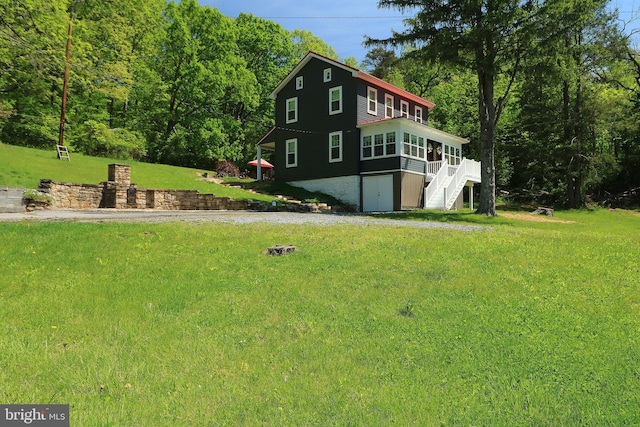 view of side of property featuring a sunroom, a lawn, stairway, and a wooded view